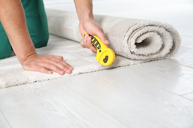 Man cutting new carpet flooring indoors, closeup. Space for text