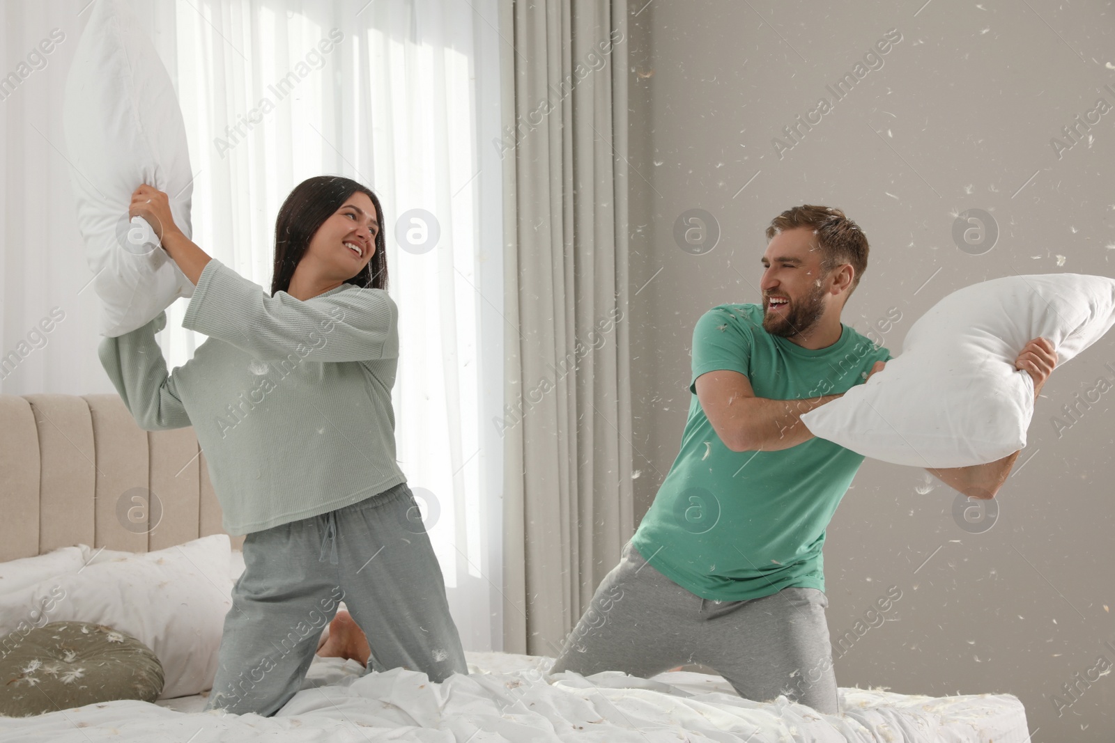 Photo of Happy young couple having fun pillow fight in bedroom