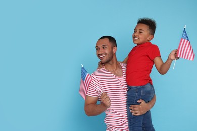 Photo of 4th of July - Independence Day of USA. Happy man and his son with American flags on light blue background, space for text