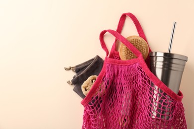 Photo of Fishnet bag with different items on beige background, top view and space for text. Conscious consumption