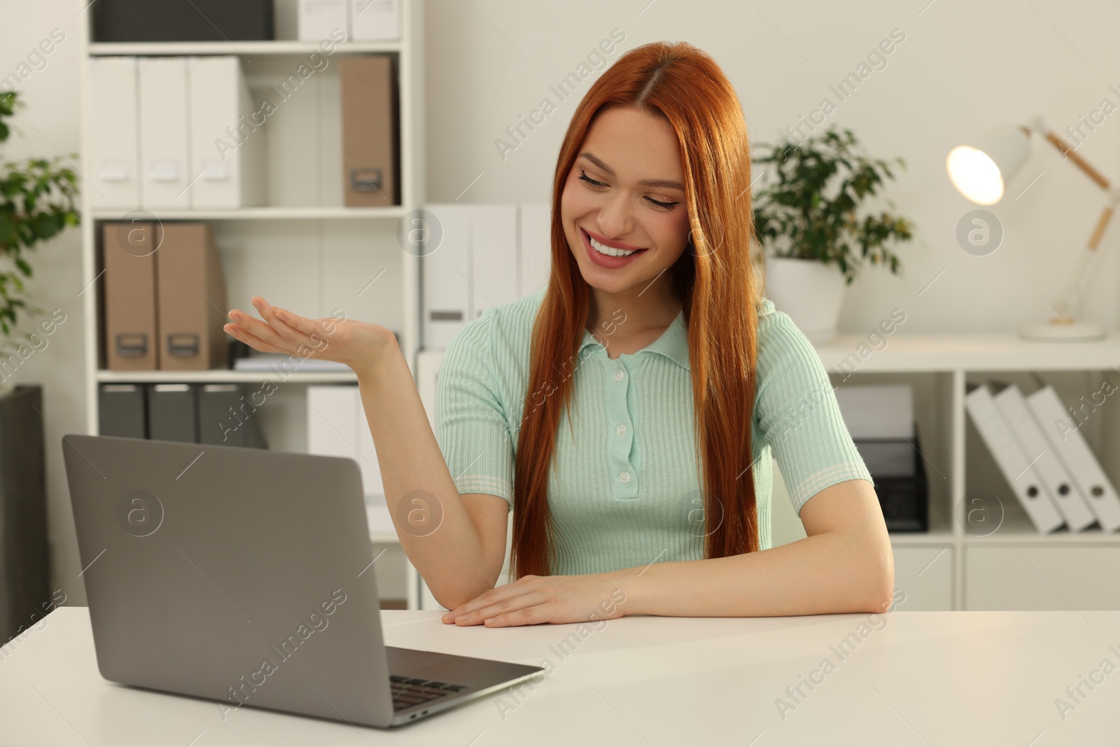 Photo of Young woman having video chat via laptop at table in office