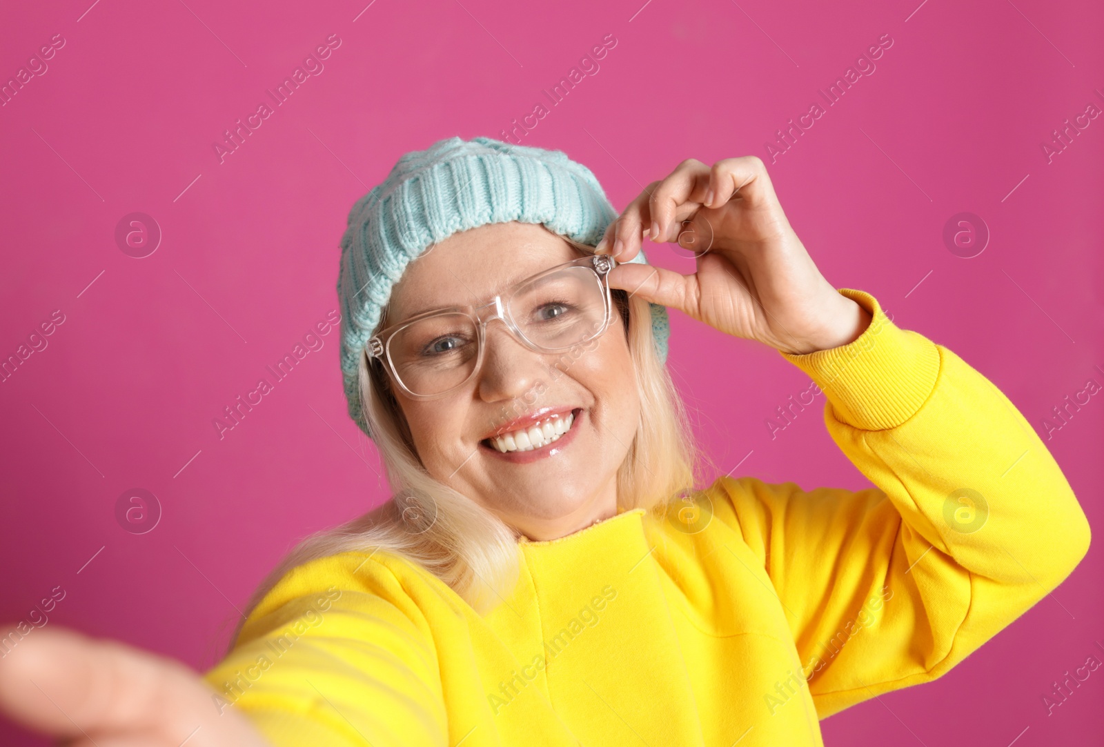 Photo of Mature woman in hipster outfit taking selfie on color background