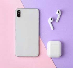 Photo of Wireless earphones, mobile phone and charging case on color background, flat lay