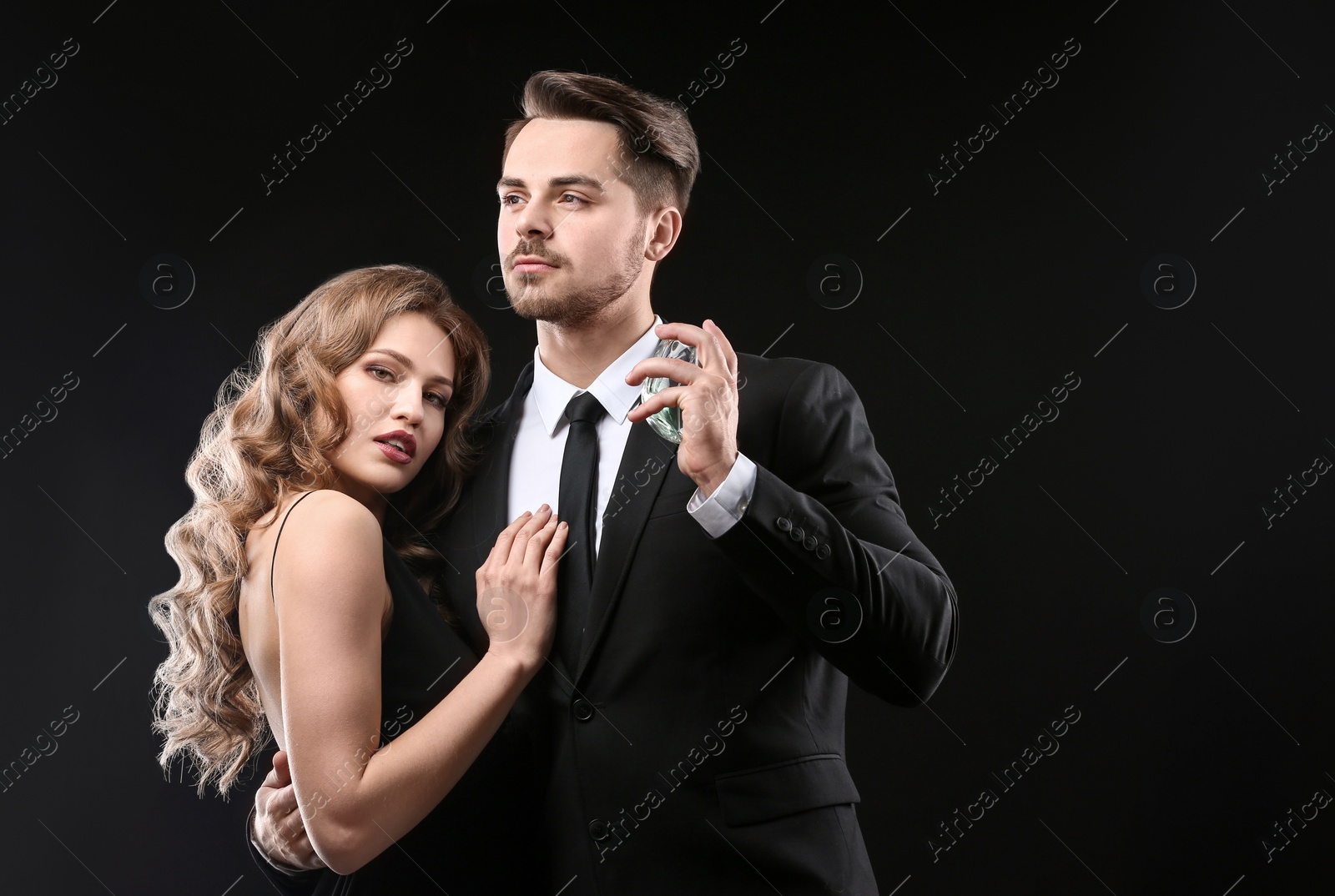 Photo of Passionate woman and handsome man using perfume on black background