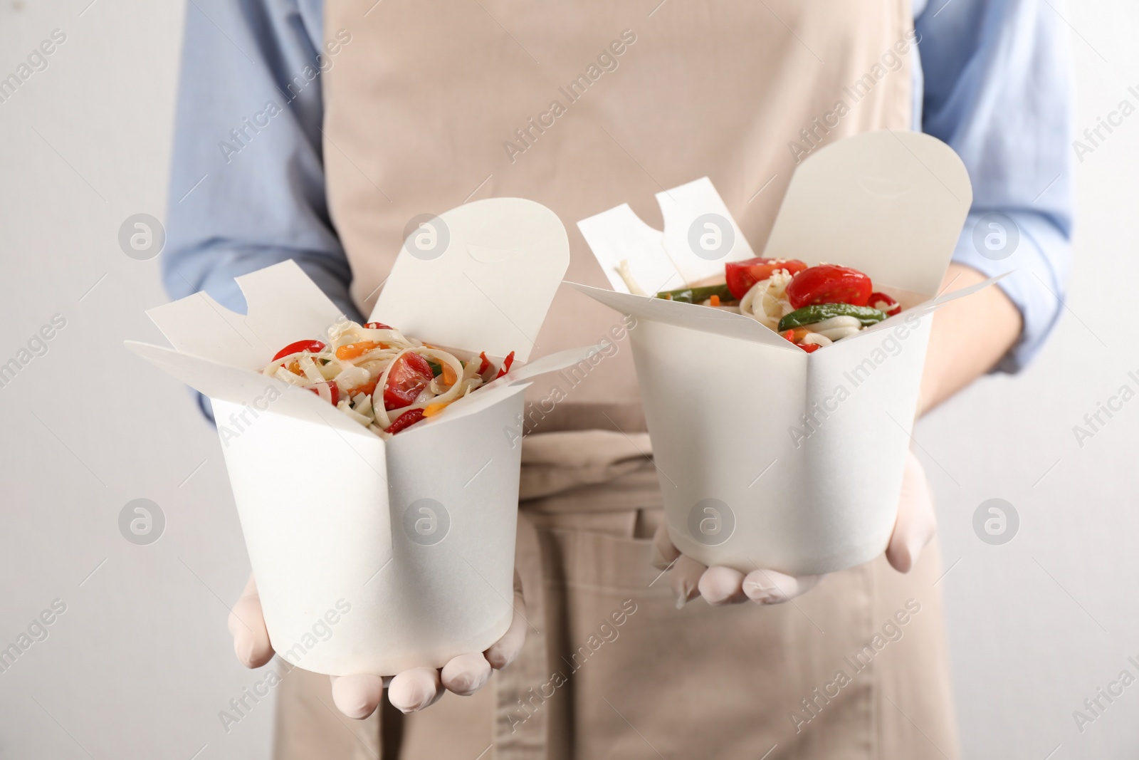 Photo of Chef holding boxes of vegetarian wok noodles on light background, closeup