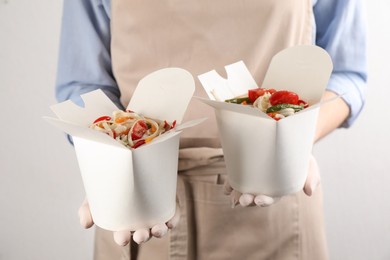 Photo of Chef holding boxes of vegetarian wok noodles on light background, closeup