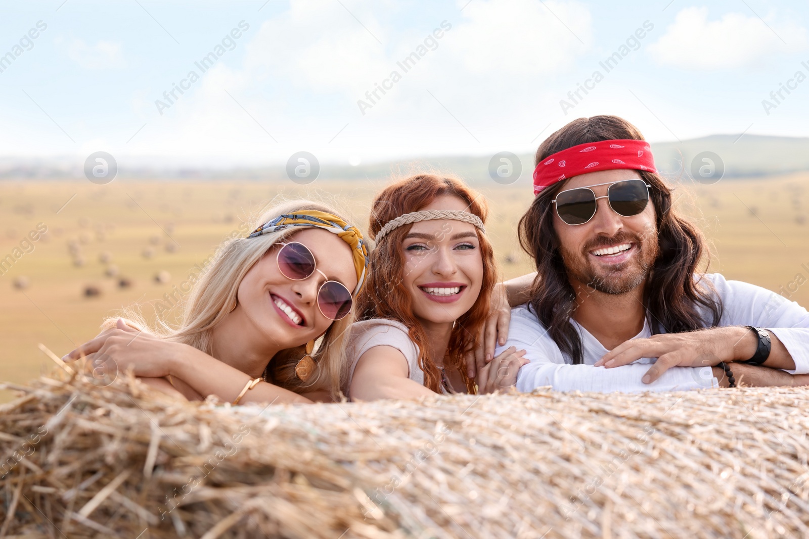 Photo of Happy hippie friends near hay bale in field