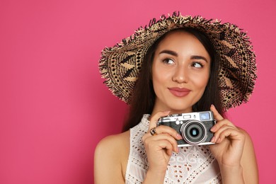 Beautiful young woman with straw hat and camera on crimson background, space for text. Stylish headdress