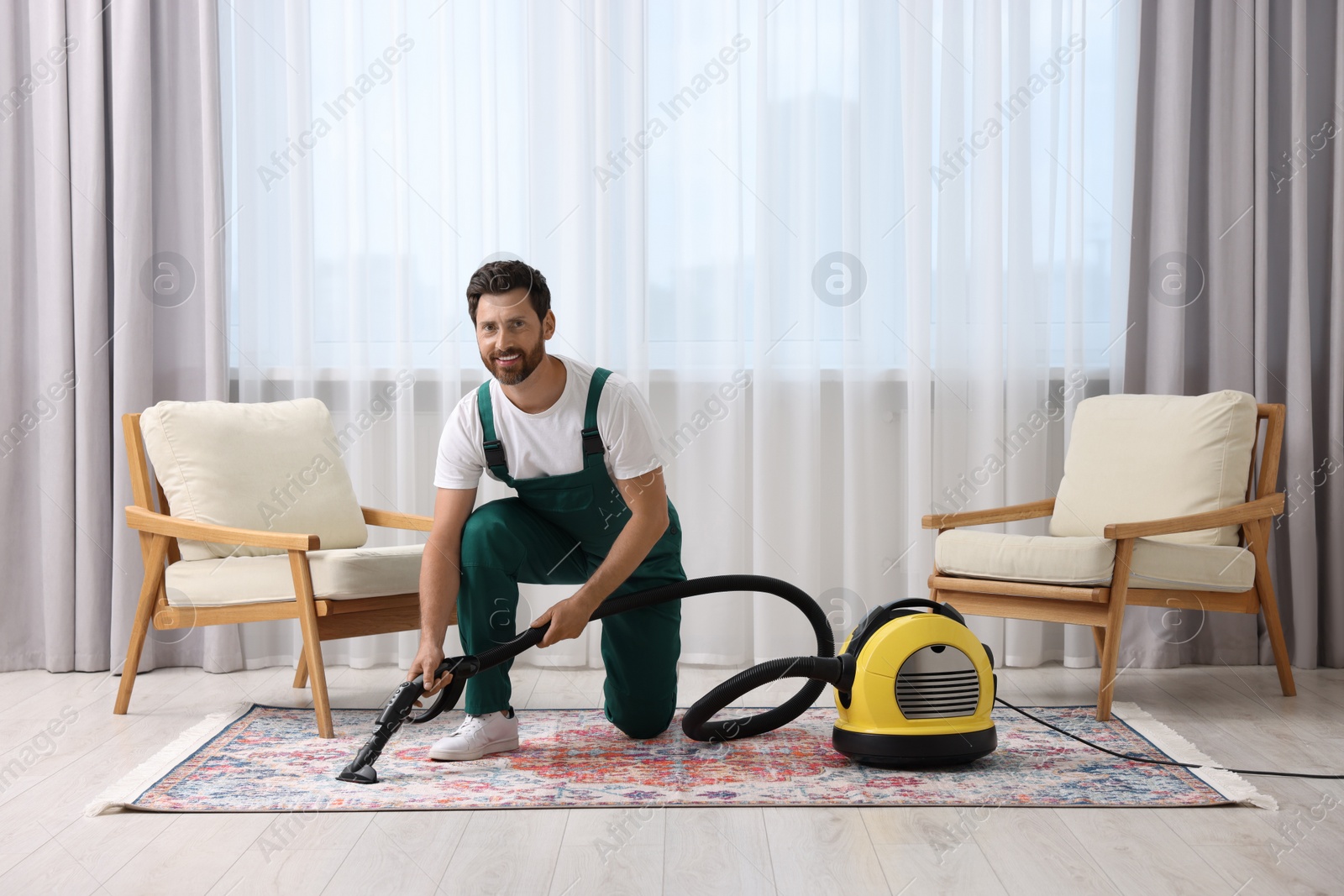 Photo of Dry cleaner's employee hoovering carpet with vacuum cleaner in room