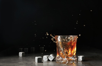 Photo of Glass with liquor splash and whiskey stones on table