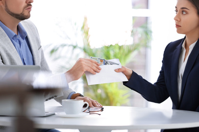 Woman giving bribe to man at table indoors, closeup