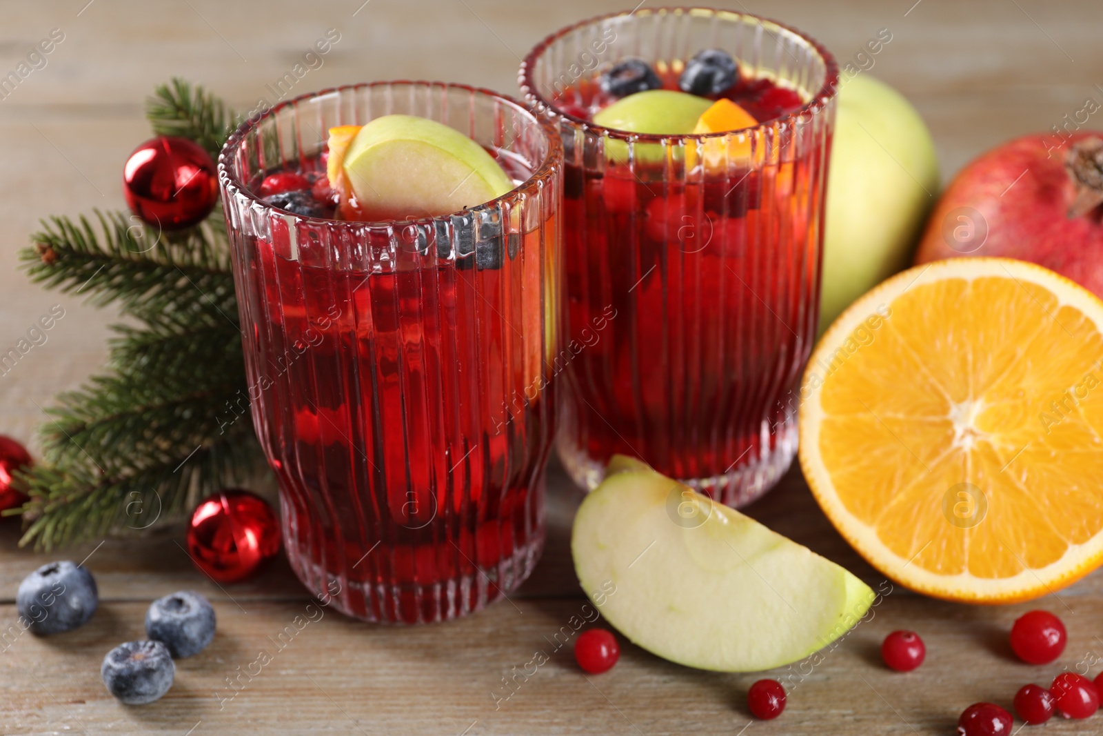 Photo of Aromatic Sangria drink in glasses, ingredients and Christmas decor on wooden table