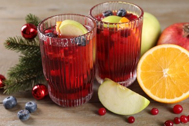 Photo of Aromatic Sangria drink in glasses, ingredients and Christmas decor on wooden table