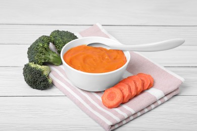 Photo of Bowl with healthy baby food, spoon and ingredients on white wooden table