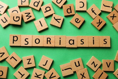 Word Psoriasis made of wooden squares with letters on green background, flat lay