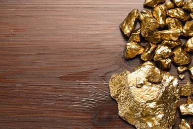Photo of Pile of shiny gold nuggets on wooden table, flat lay. Space for text