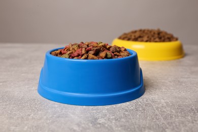 Dry food in pet bowls on grey surface