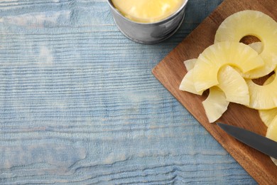 Photo of Tasty canned pineapple on light blue wooden table, flat lay. Space for text