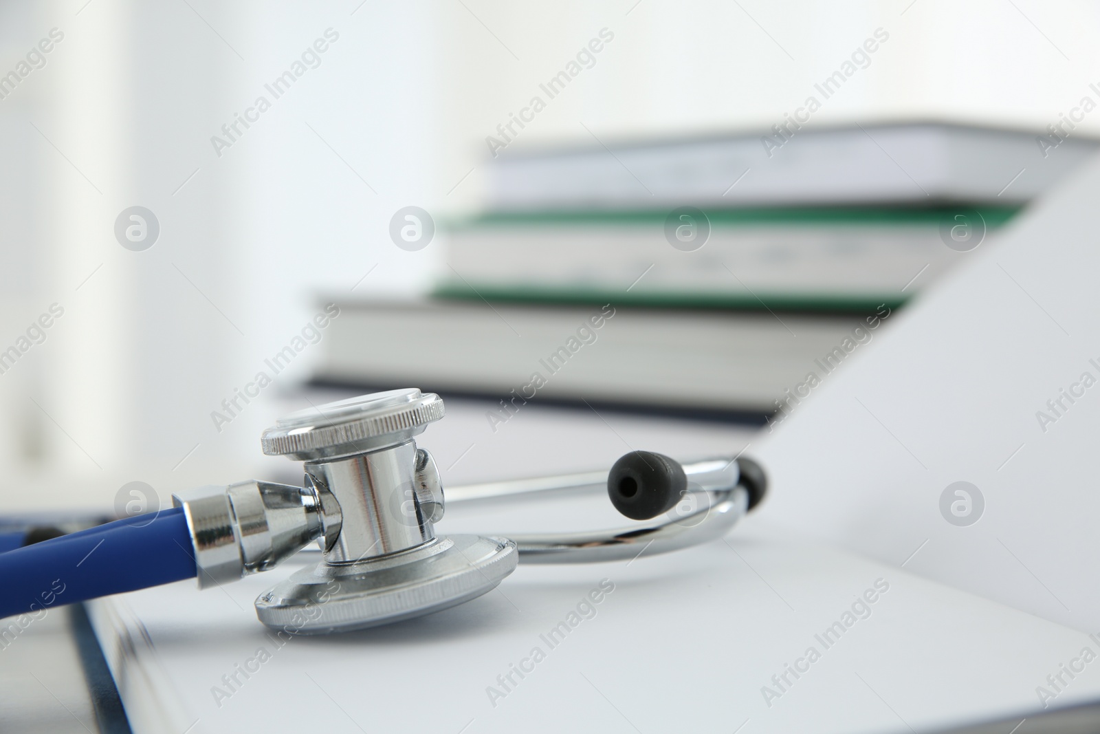 Photo of One new medical stethoscope and books on white table, closeup