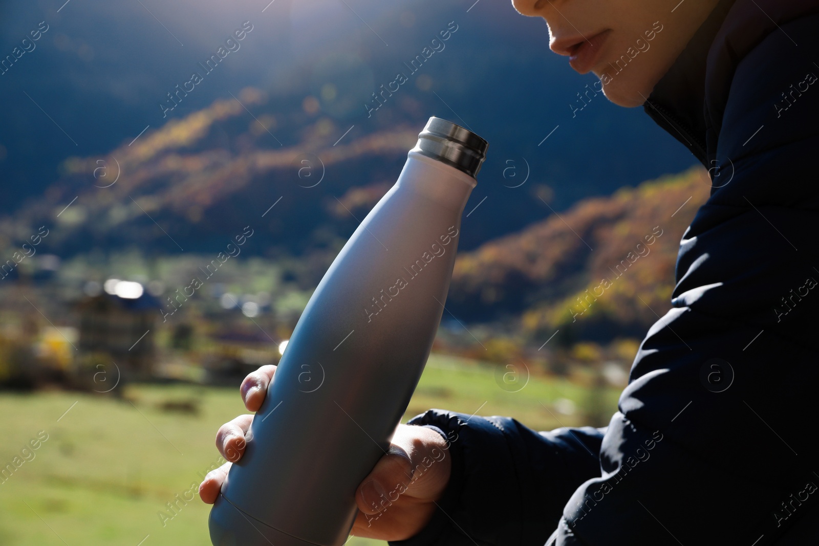 Photo of Boy holding thermo bottle with drink in mountains on sunny day, closeup