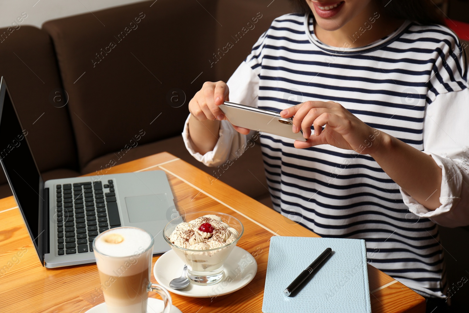 Photo of Young blogger taking picture of dessert and latte at table in cafe, closeup