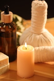 Photo of Spa composition. Cosmetic products, herbal bags and burning candle on wooden table, closeup