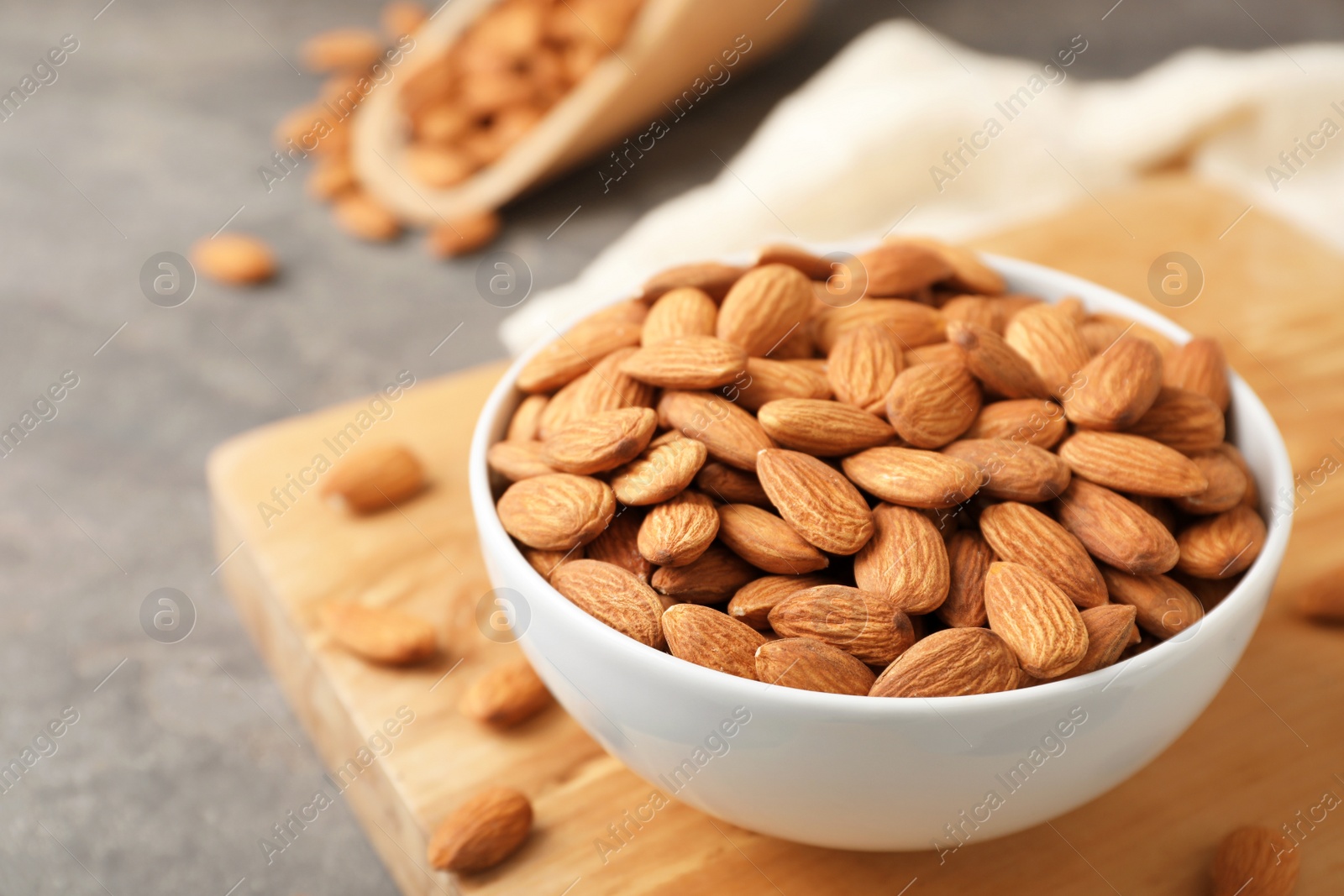 Photo of Wooden board with tasty organic almond nuts in bowl on table