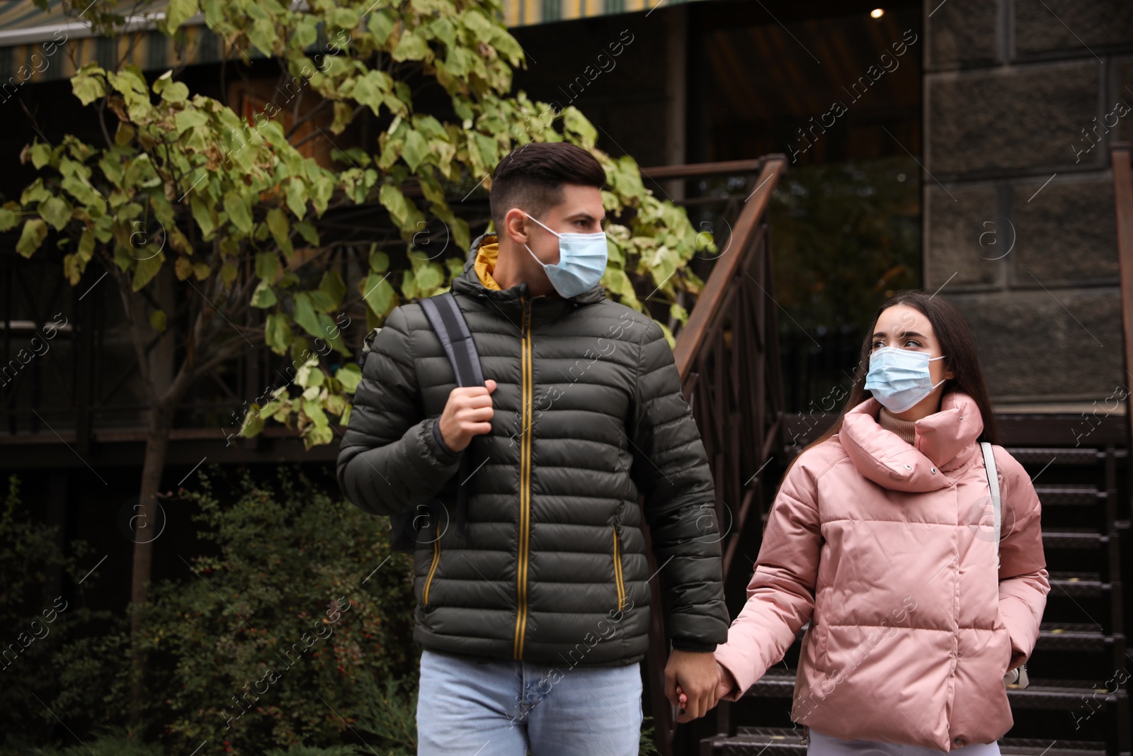 Photo of Couple in medical face masks walking outdoors. Personal protection during COVID-19 pandemic