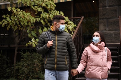 Photo of Couple in medical face masks walking outdoors. Personal protection during COVID-19 pandemic