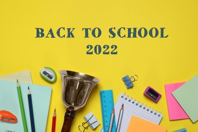 Back to school 2022. Different stationery and bell on yellow background, flat lay