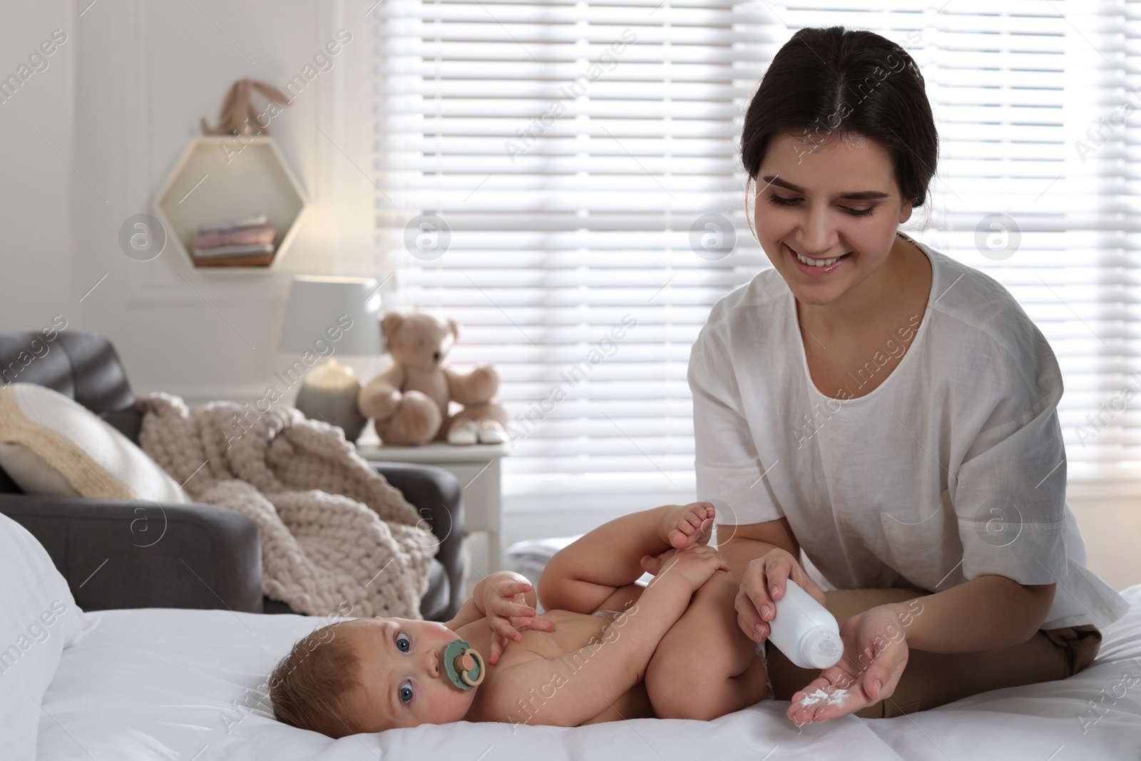 Photo of Mother with dusting powder near her cute baby at home, space for text