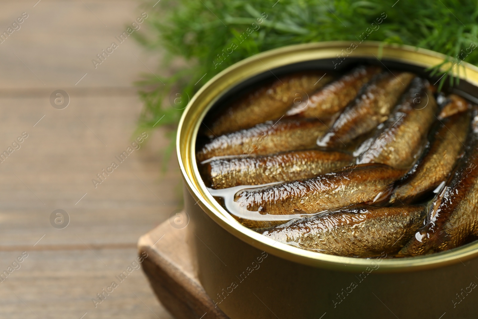 Photo of Tin can with tasty sprats on wooden table, closeup. Space for text