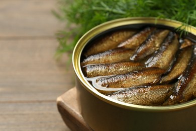 Tin can with tasty sprats on wooden table, closeup. Space for text