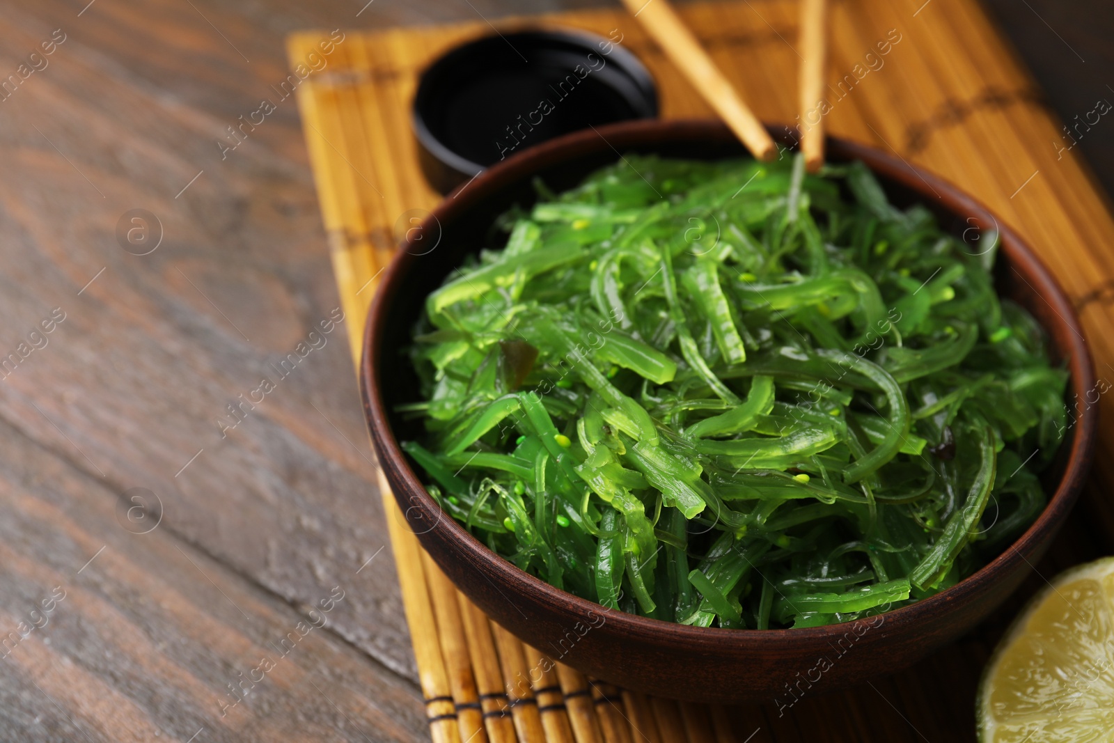 Photo of Tasty seaweed salad in bowl served on wooden table, closeup