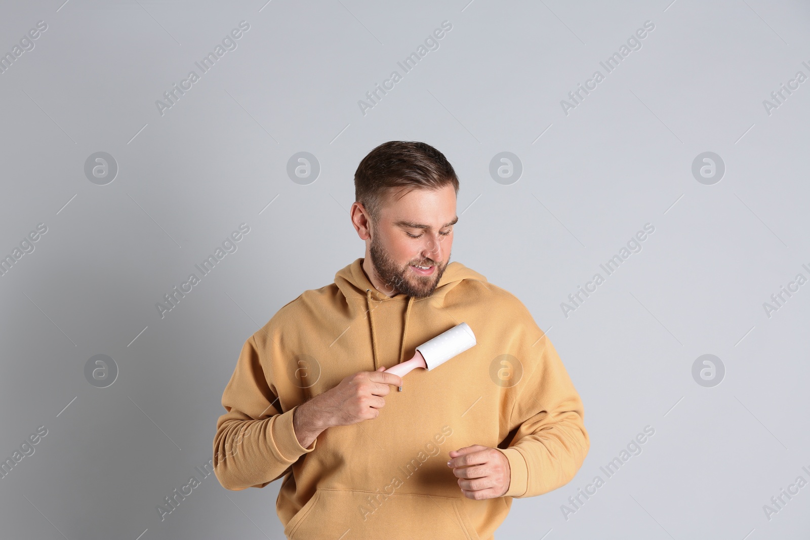 Photo of Young man cleaning clothes with lint roller on grey background