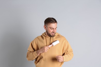 Photo of Young man cleaning clothes with lint roller on grey background