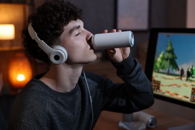 Photo of Young man with energy drink and headphones playing video game at home