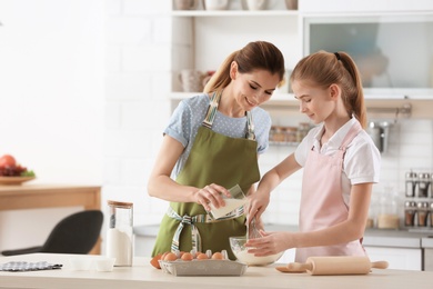 Photo of Mother and her daughter making dough at table in kitchen