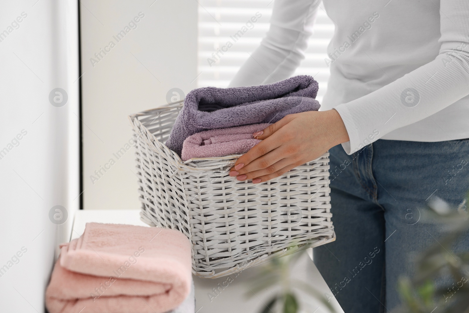 Photo of Woman with laundry basket of clean towels indoors, closeup