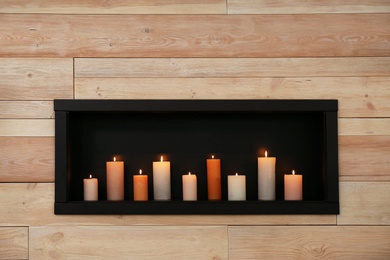 Photo of Burning candles on shelf in wooden wall