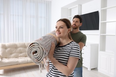 Smiling couple holding rolled carpet in room