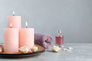 Photo of Burning candles, roses, essential oil and towel on grey table