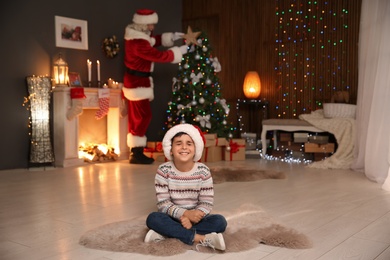 Photo of Little child waiting while Santa Claus decorating Christmas tree at home