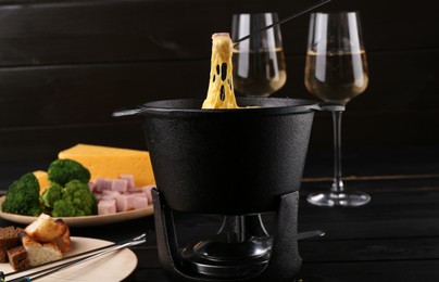 Photo of Dipping piece of ham into fondue pot with melted cheese on table