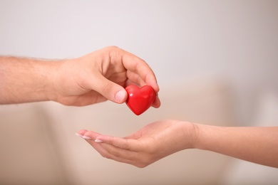 Photo of Man giving red heart to woman on blurred background, closeup. Donation concept