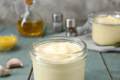 Photo of Delicious homemade mayonnaise in jar and ingredients on light blue wooden table, closeup