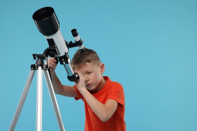 Little boy looking at stars through telescope on light blue background, space for text