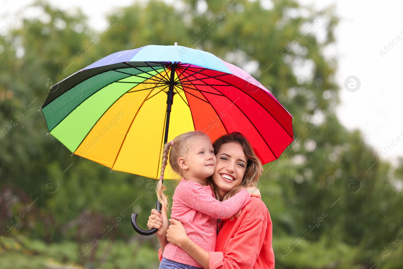 Photo of Happy mother and daughter with bright umbrella under rain outdoors