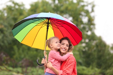 Happy mother and daughter with bright umbrella under rain outdoors