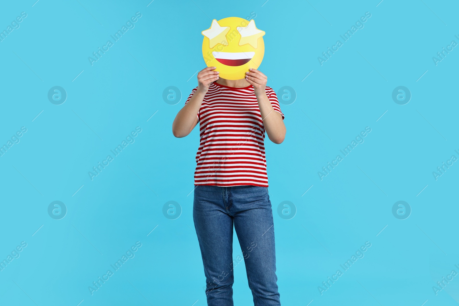 Photo of Woman holding emoticon with stars instead of eyes on light blue background